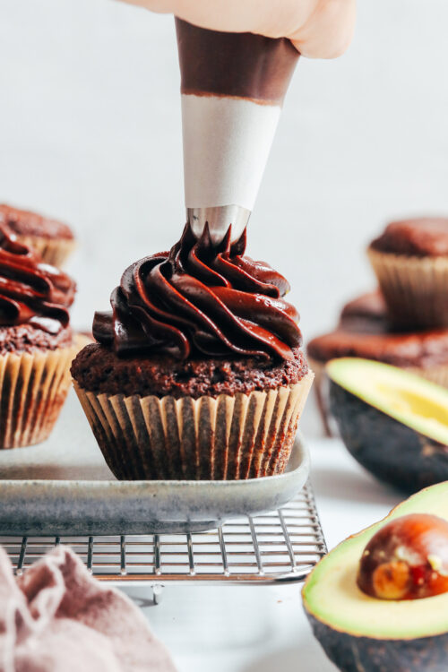 Piping chocolate avocado frosting onto a cupcake